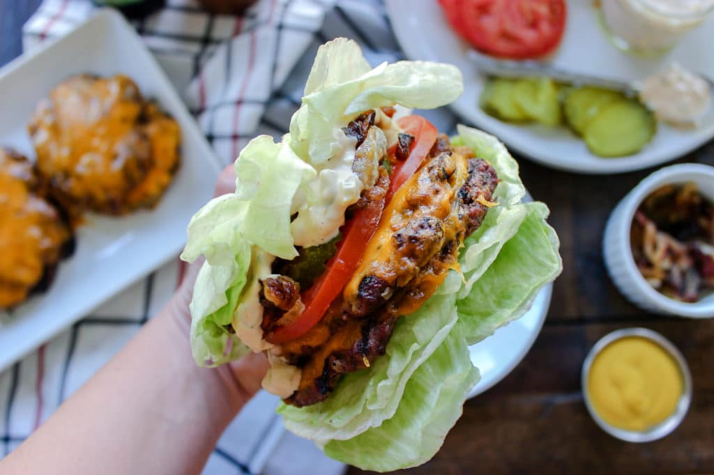 A hand holding a lettuce wrapped smash burger.