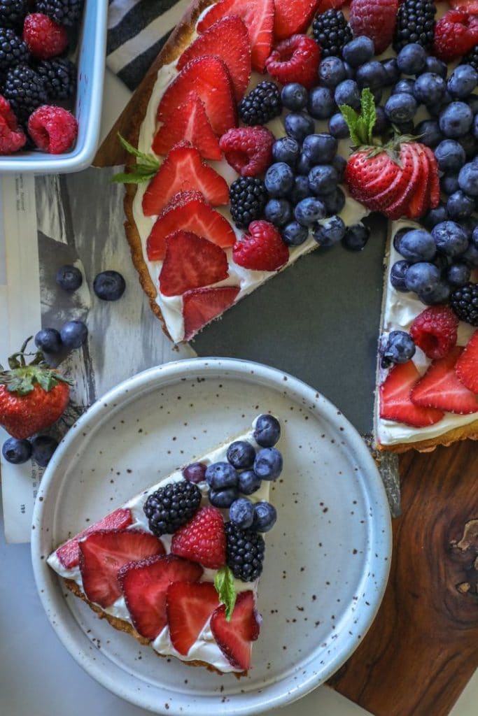 Large keto sugar cookie with decorated fruit on top, sliced into pieces.