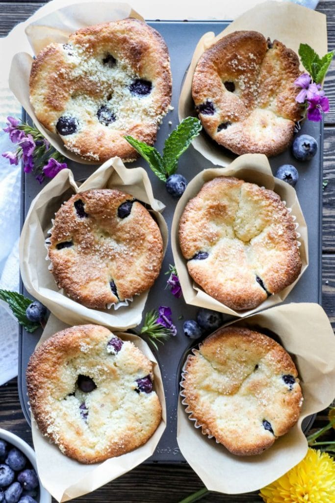 Easy Almond Flour Keto Blueberry Muffins in a muffin tin with blueberries and flowers. 