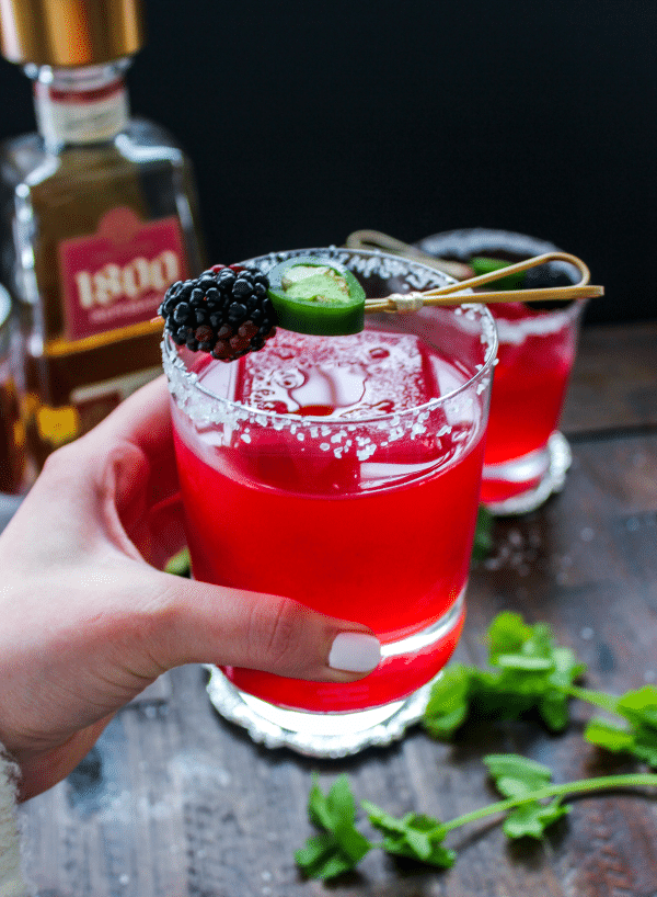 A person holding a glass with a jalapeno blackberry margarita in it.