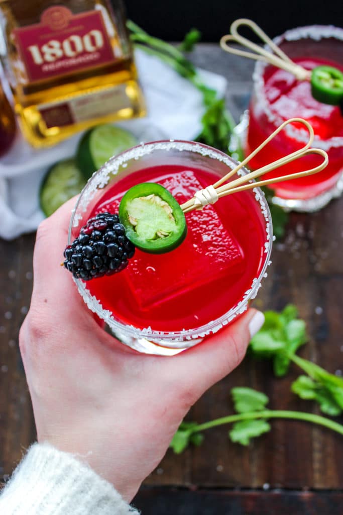 A hand holding a low carb blackberry jalapeno margarita