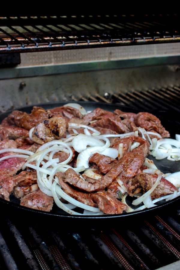 Carne Asada cooking in a cast iron pan on the grill. 