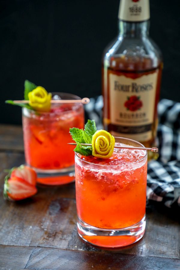 A close up of a bottle and a glass of whiskey on a table, with Strawberry and Whiskey smash