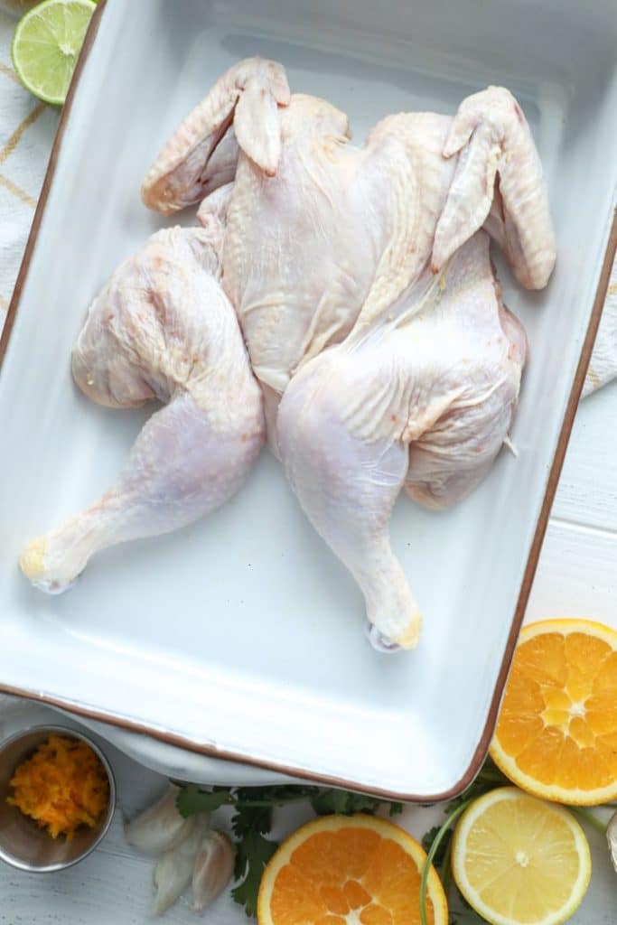 Raw whole chicken in a baking pan waiting for a mojo marinade. 