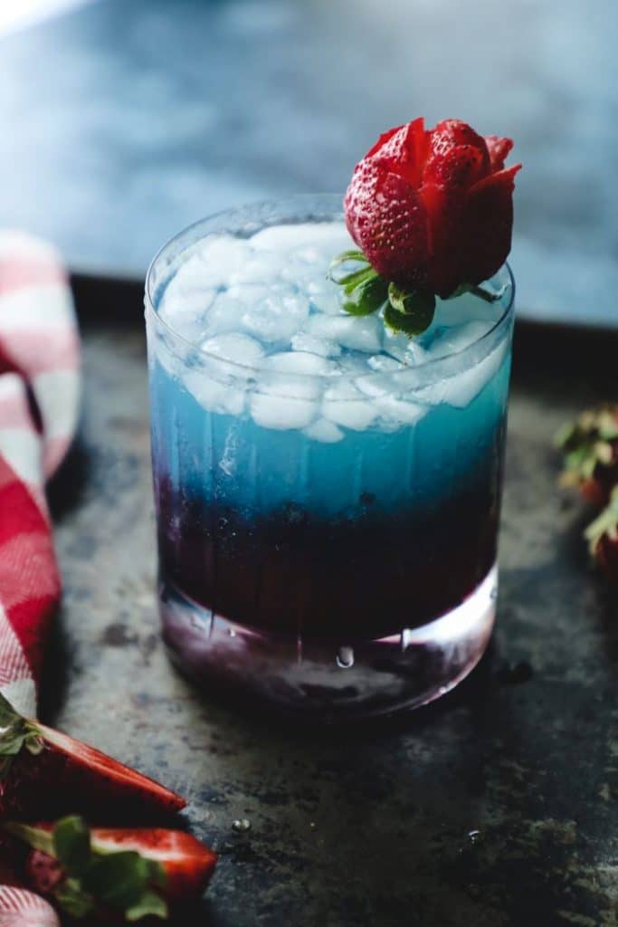 Red white and blue cocktail with a strawberry rose garnish