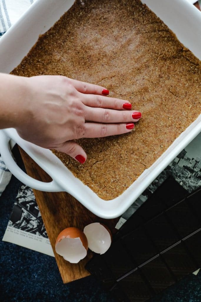 A hand patting down the crust into the pan