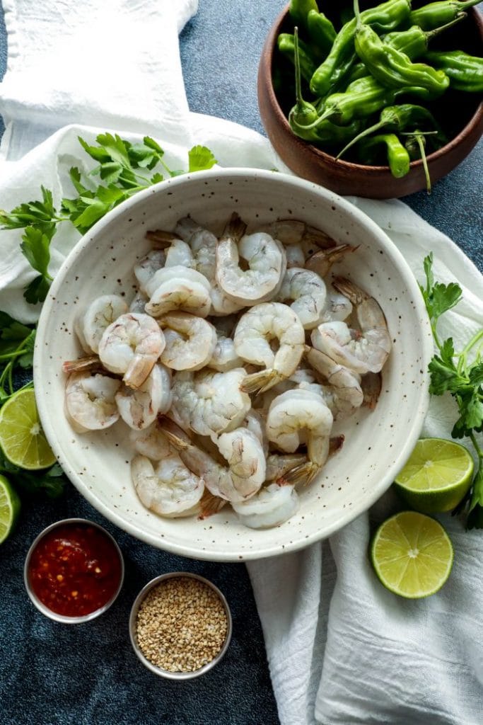 Raw shrimp and seasonings in a bowl on a white towel.