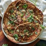 A large plate with 8 round flatbreads with parsley, garlic, and butter over the top.