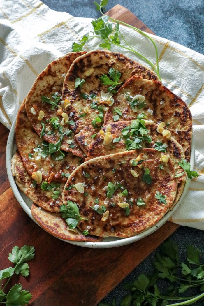 A large plate with 8 round flatbreads with parsley, garlic, and butter over the top.