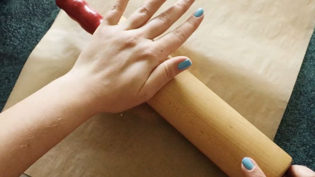 Parchment paper covered dough being rolled out with a rolling pin