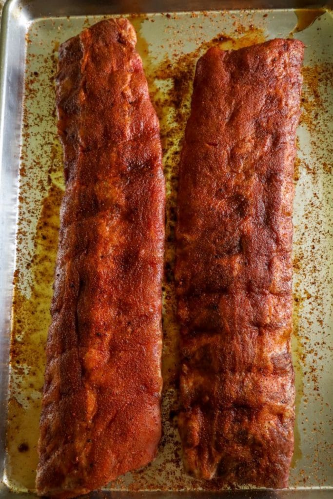 Raw ribs prepped with a dry rub and resting on a baking sheet