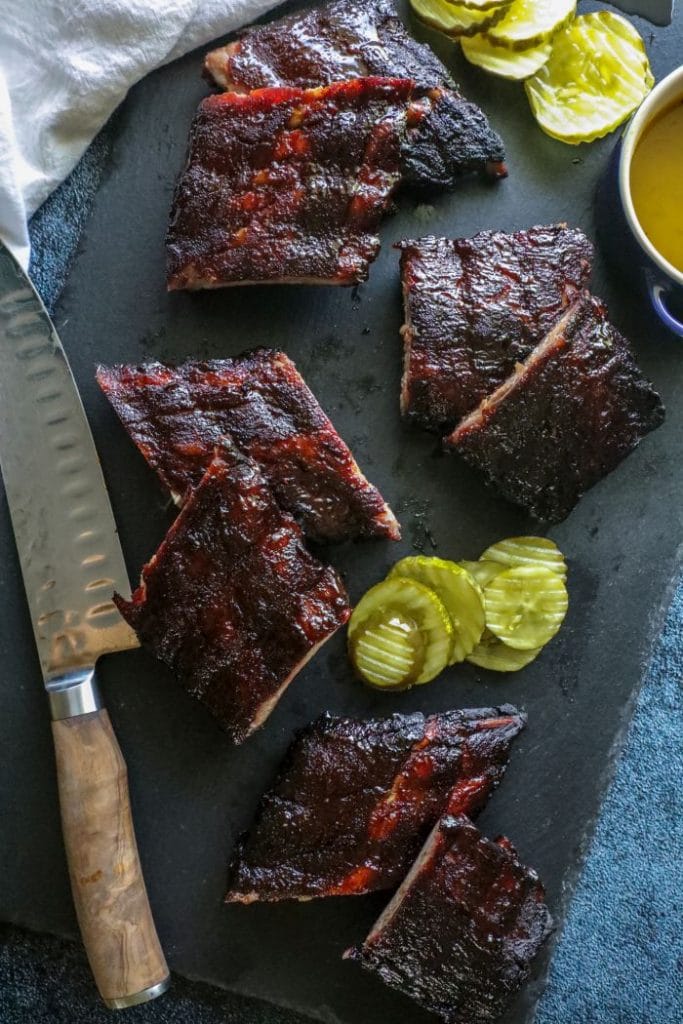 Sliced up rib racks on a cutting board with a knife and pickles