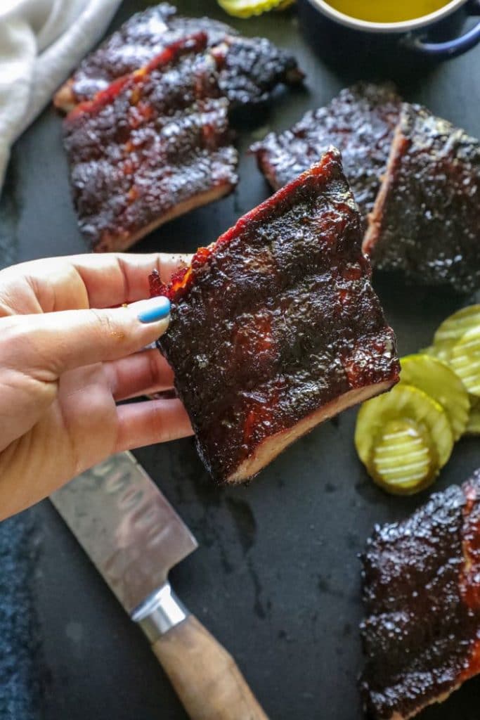 A person holding a rack of ribs over a plate. 