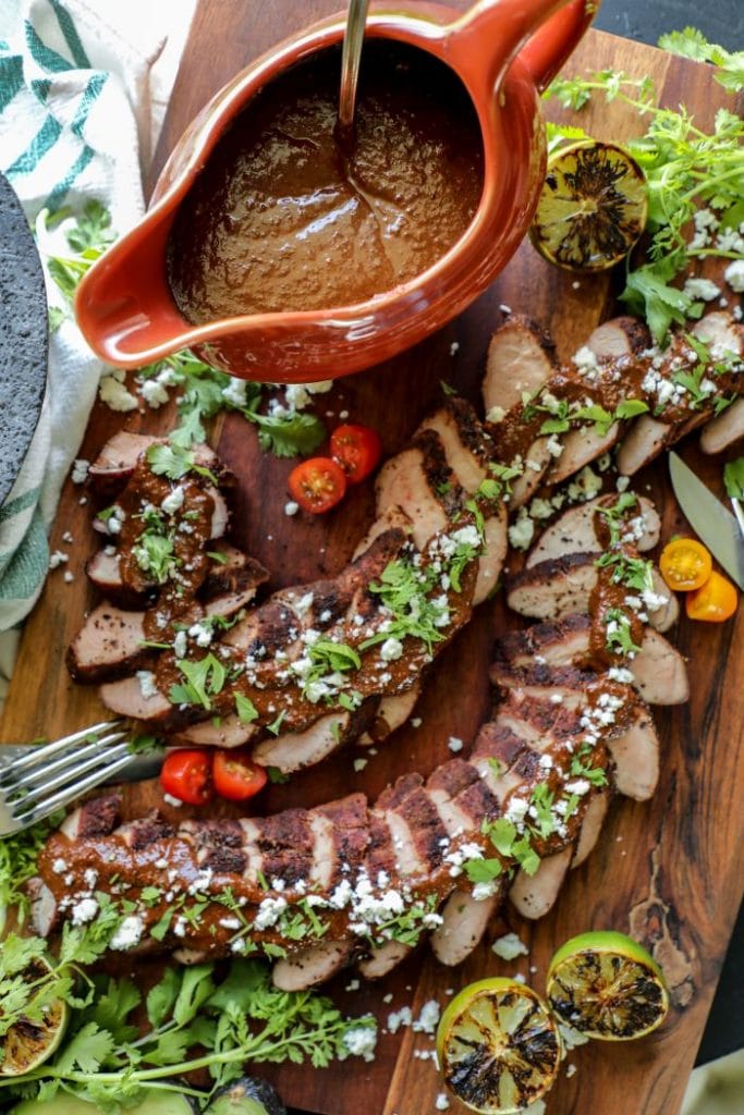 Gravy boat of mole sauce with a platter of layered sliced pork tenderloin with mole sauce over the top