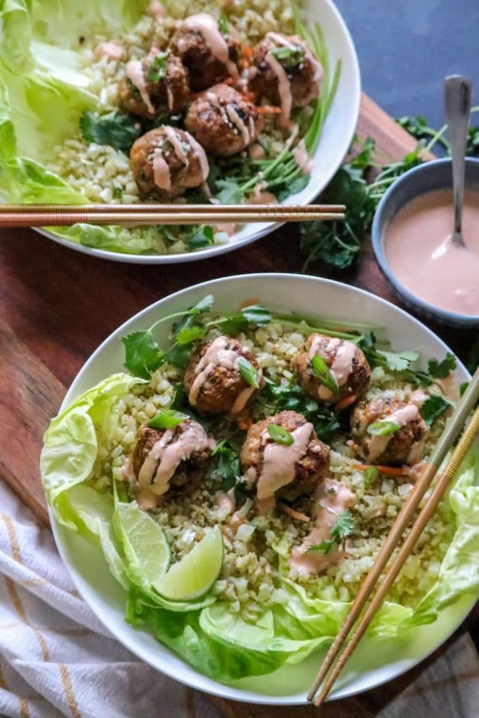 Lettuce cups and cauliflower rice in a bowl with egg roll meatballs and chopsticks. 