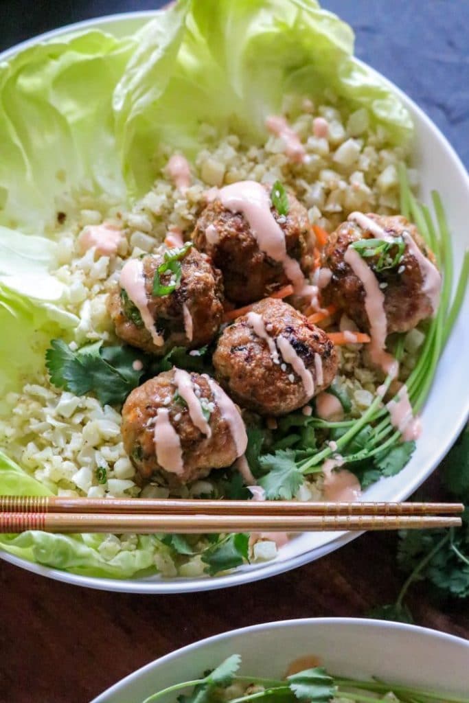 Lettuce cups and cauliflower rice in a bowl with egg roll meatballs and chopsticks. 