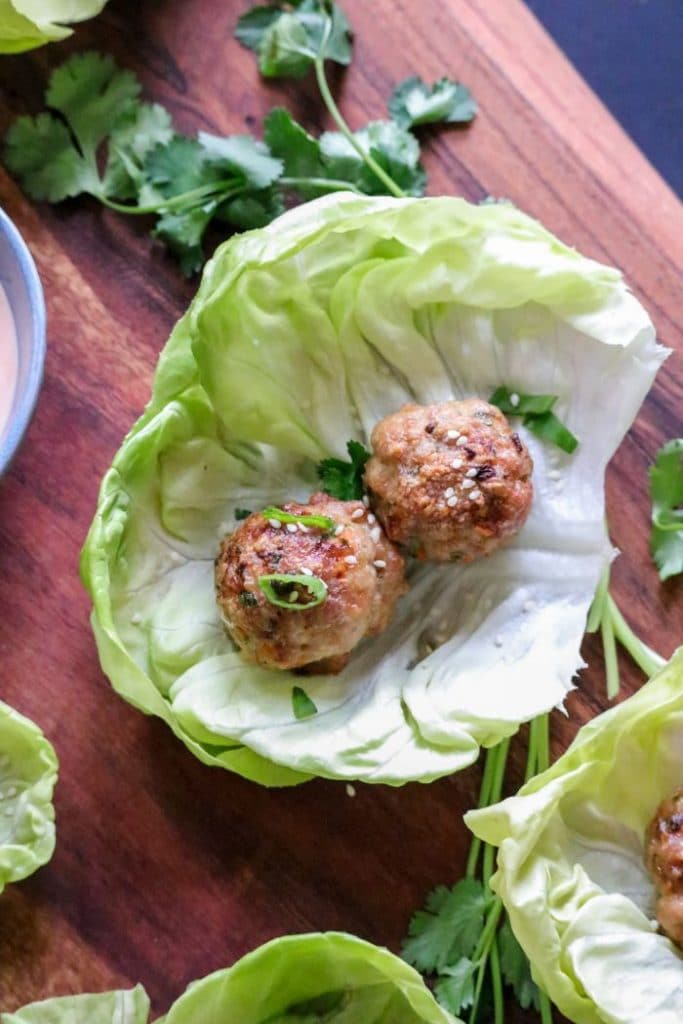 A lettuce cup sitting on top of a wooden table, with an egg roll meatball