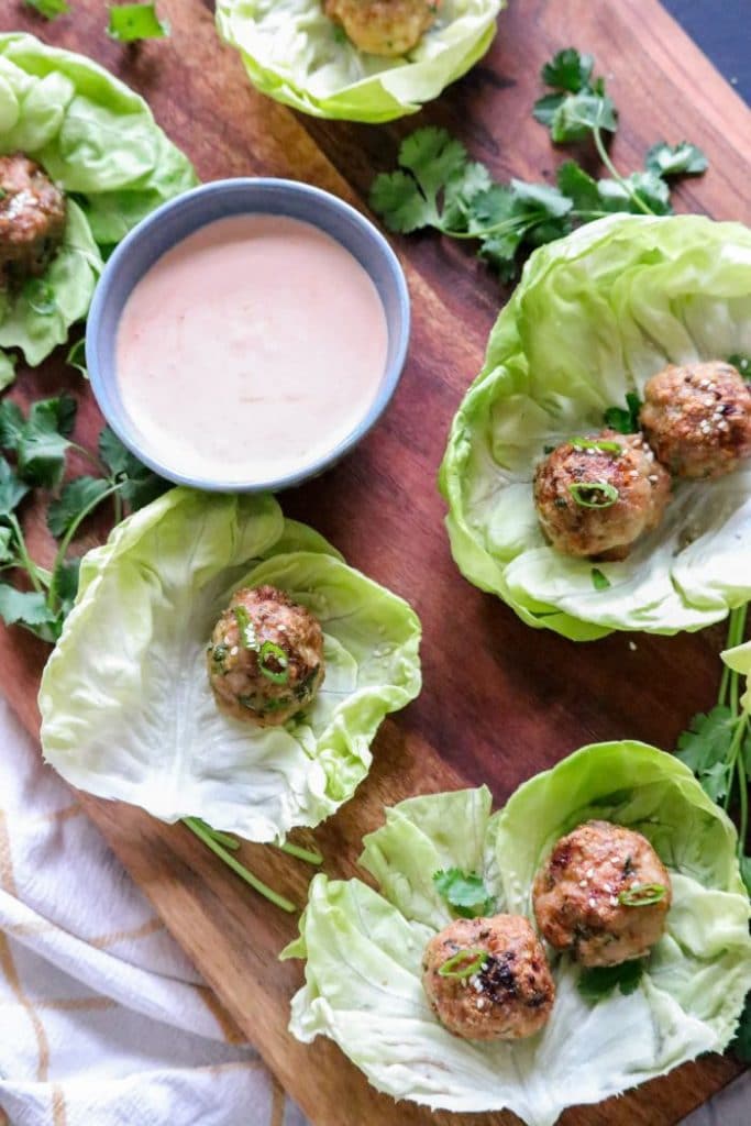 A bunch of food on a table, with Lettuce cups and meatballs placed inside. 