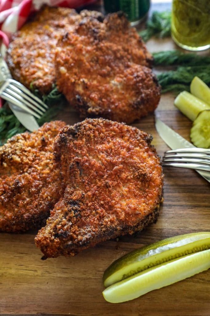 Smoked Dill Pickle Brined Pork Chops on a cutting board with pickles and a knife.