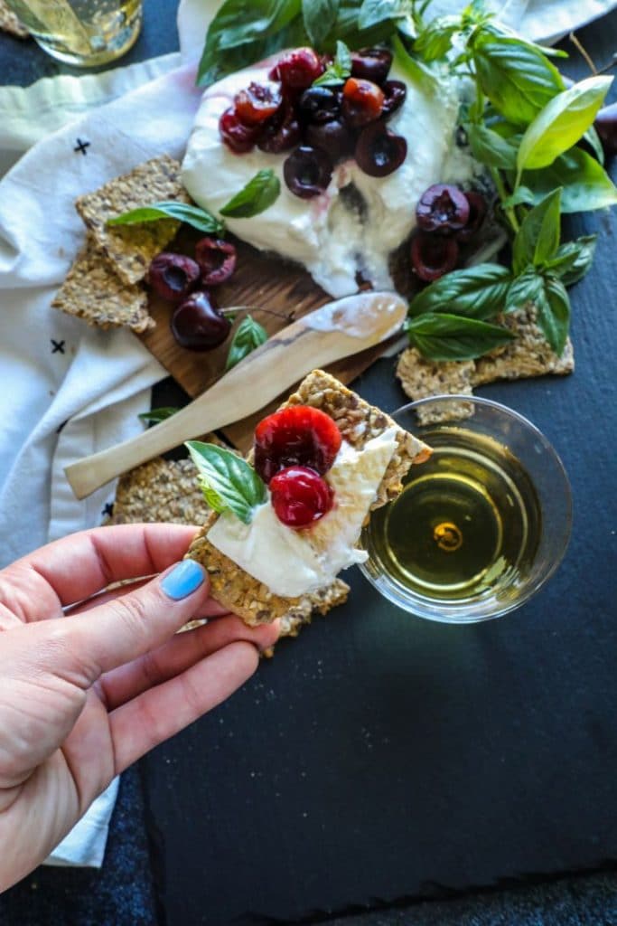 Cedar Plank Smoked Burrata with cherries and basil on a cracker.