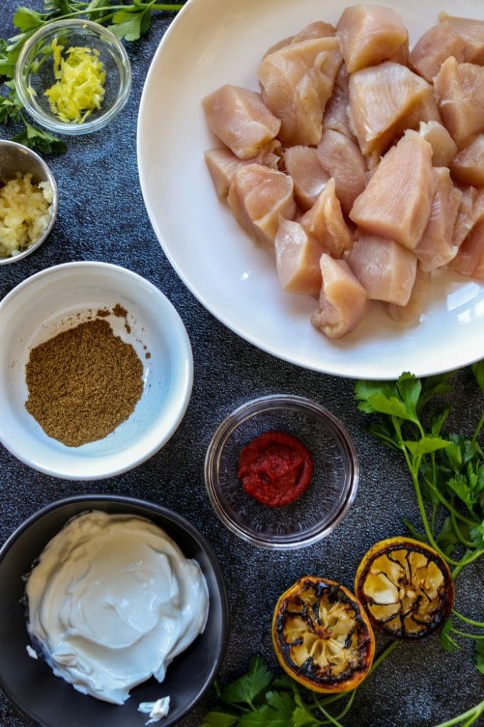 Grilled Butter chicken ingredient in separate bowls on a blue table.