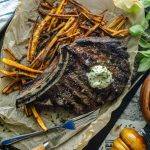 Keto Steak Frites with a bone in ribeye over a bed of jicama fries on a tray.