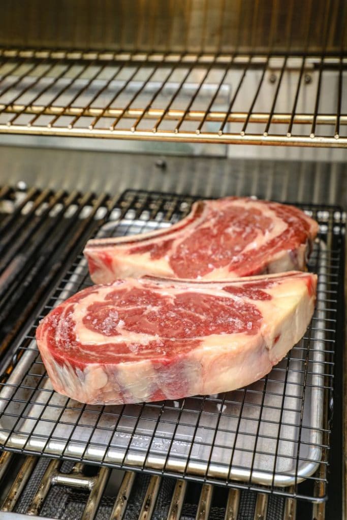 Two raw ribeyes on indirect heat on the grill.