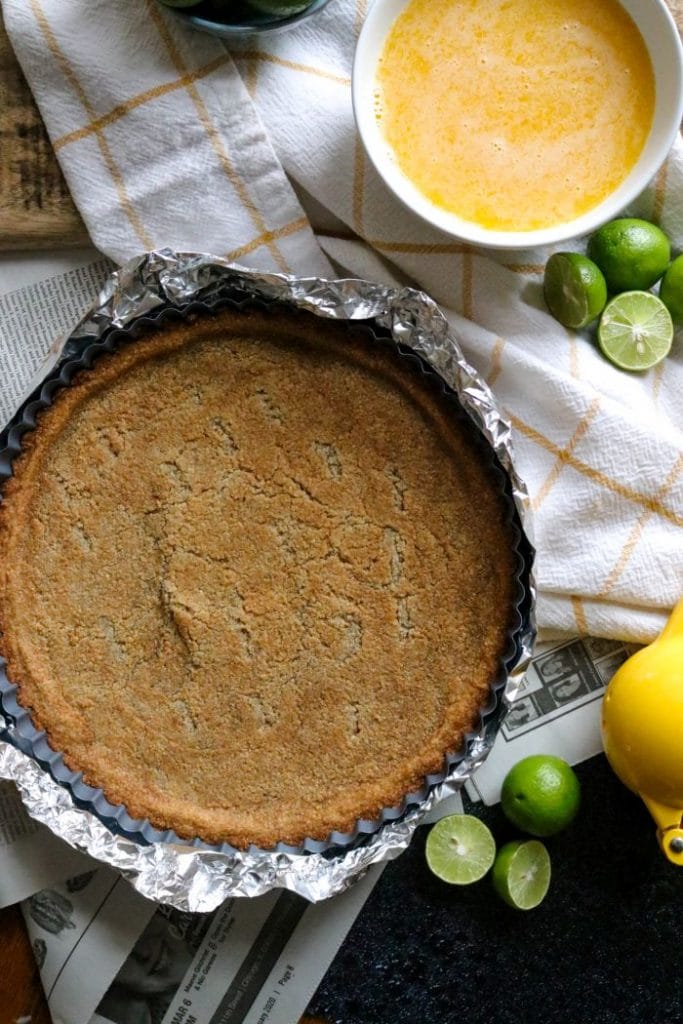 The partially baked keto key lime pie crust on a yellow towel and newspaper.