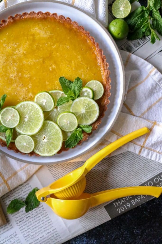 Keto key Lime Tart with lime rounds on a white plate with a yellow towel and yellow fruit juicer. 
