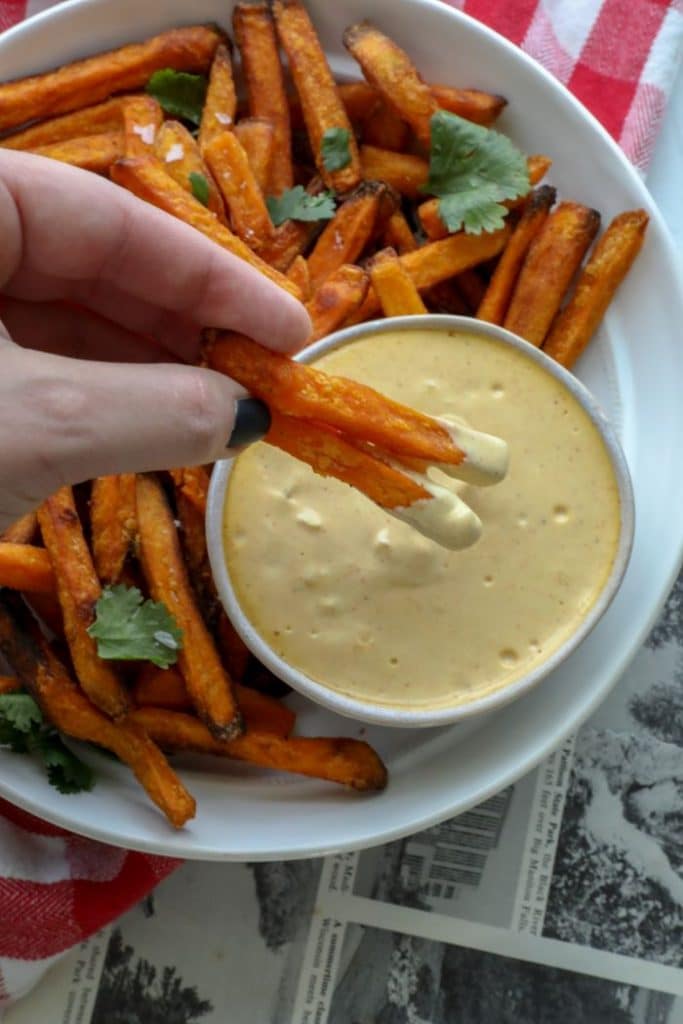 Two sweet potato fries being dipped in the keto burger sauce.