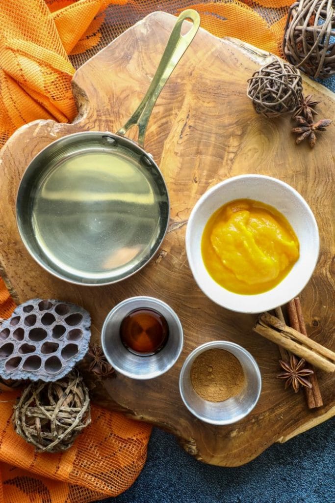 Keto Pumpkin Spice Simple Syrup ingredients on a wood platter with an orange towel.