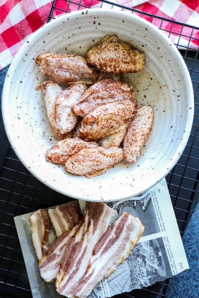 Seasoned chicken wing flats and bacon on paper on a tray.