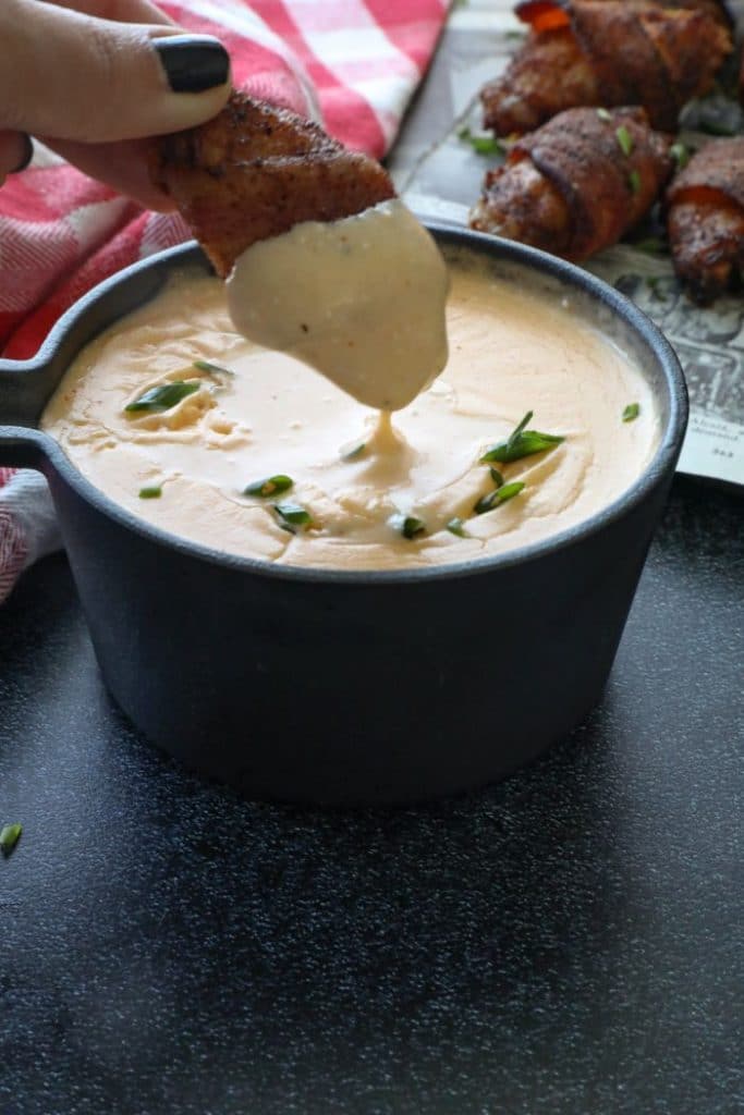 Bacon Wrapped Chicken Wings being dipped inside the cheese sauce