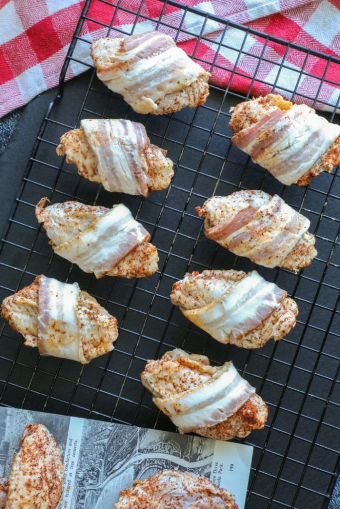 Raw chicken wing flats wrapped in bacon on a tray.