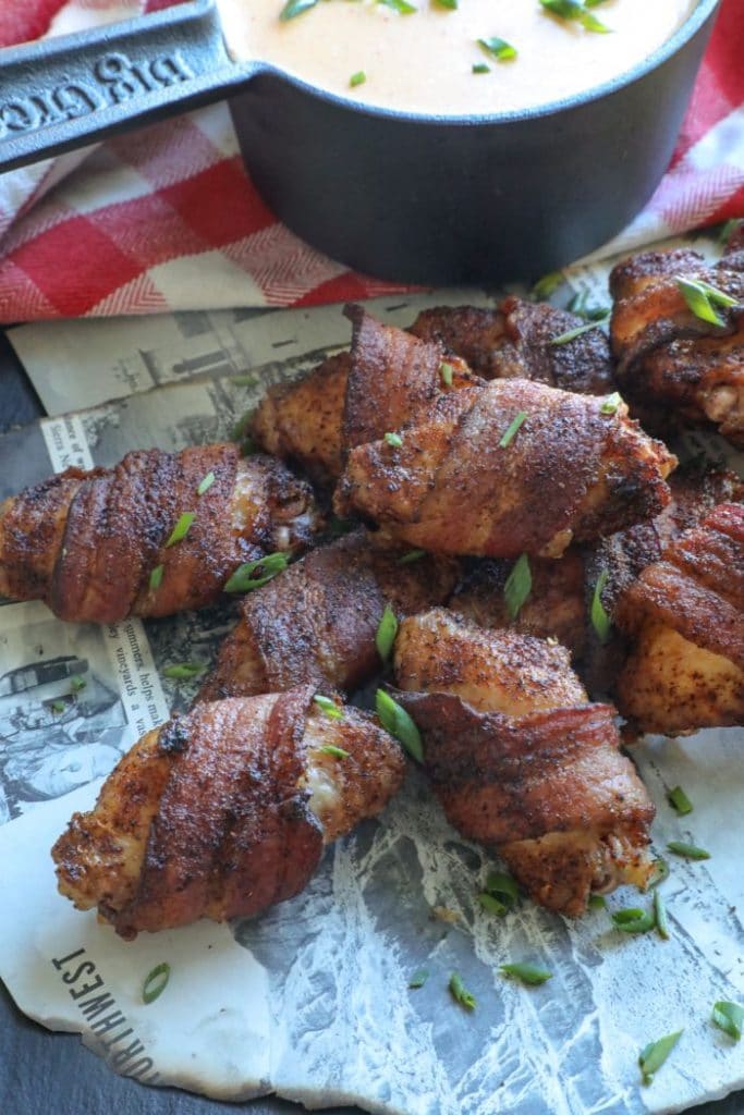 Bacon Wrapped Chicken Wings with Beer Cheese Sauce on newspaper with a red towel.