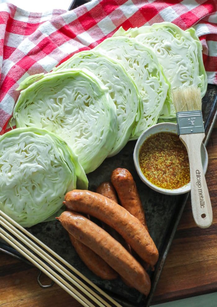 Sliced cabbage steaks and smoked sausage with skewers on a tray.