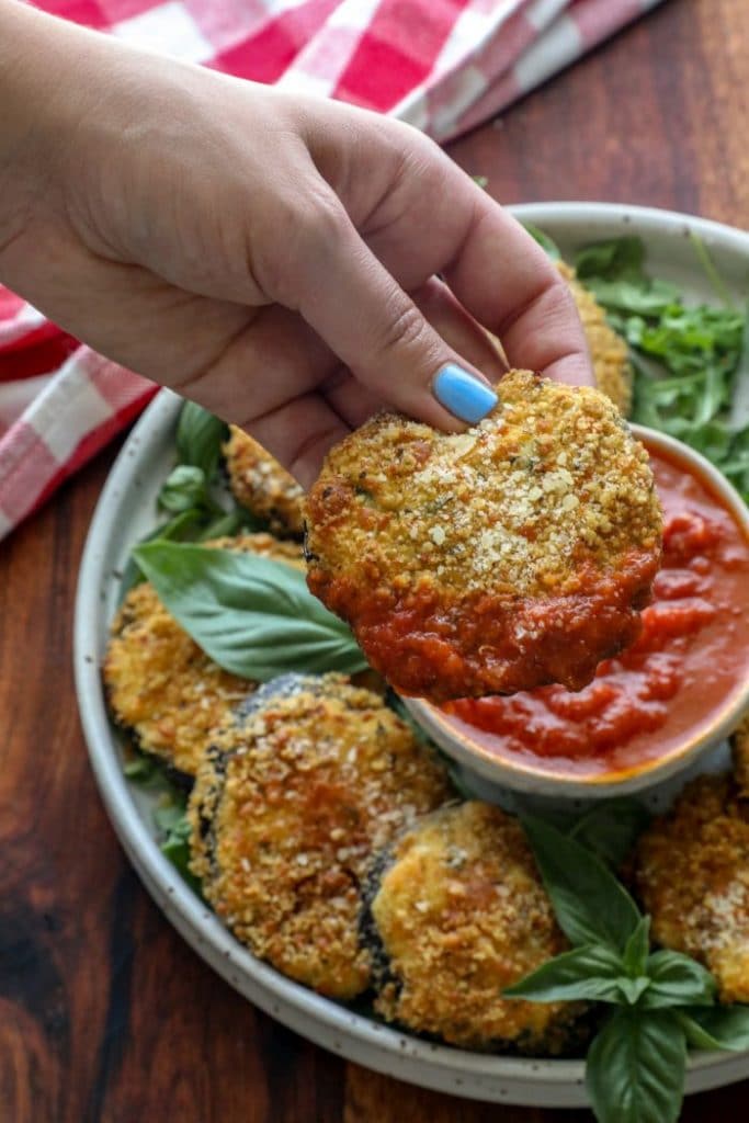 A hand dipping a Two hands holding a plate with Crispy Keto Ricotta Stuffed Eggplant Round into tomato sauce