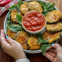 Two hands holding a plate with Crispy Keto Ricotta Stuffed Eggplant Rounds
