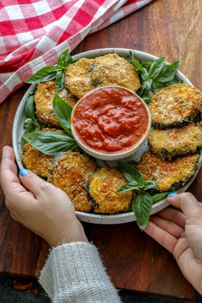 Two hands holding a plate with Crispy Keto Ricotta Stuffed Eggplant Rounds