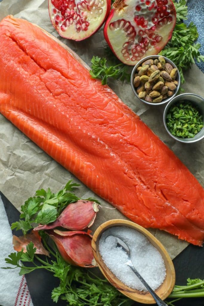 Whole side of salmon on parchment with chimichurri ingredients next to it.