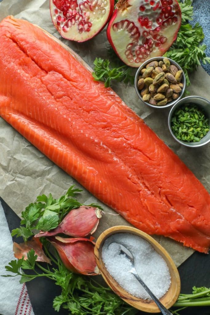 Whole side of salmon on parchment with chimichurri ingredients next to it. 