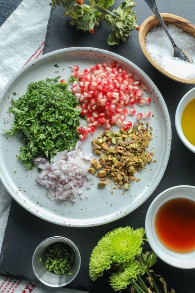 Pistachio and pomegranate chimichurri ingredients on a white plate. 