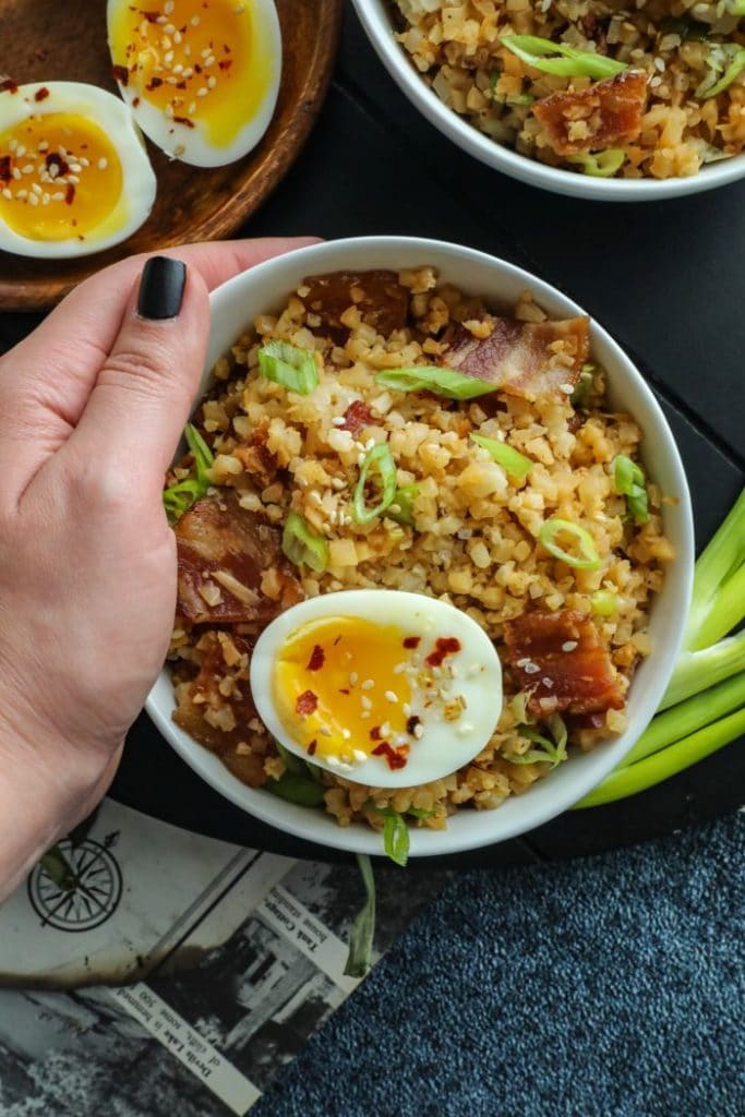 A hand holding a bowl of bacon cauliflower fried rice. 