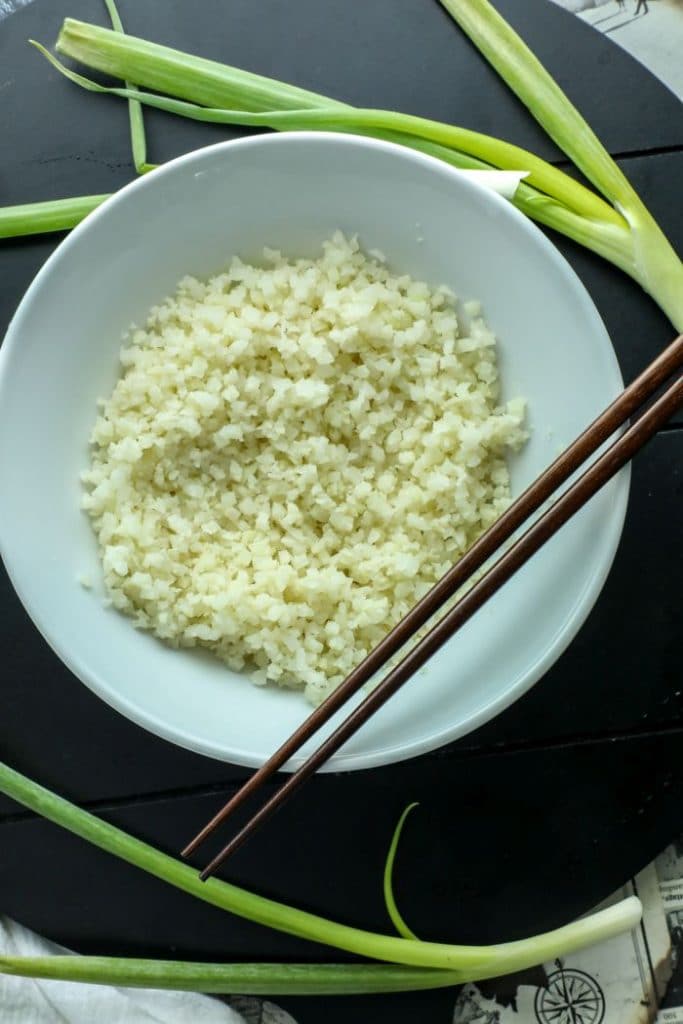 Par-cooked frozen cauliflower rice in a white bowl with brown chopsticks.