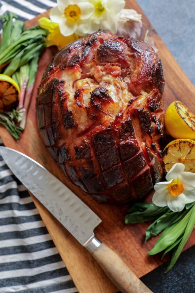 A whole low carb holiday ham on a cutting board with a knife.