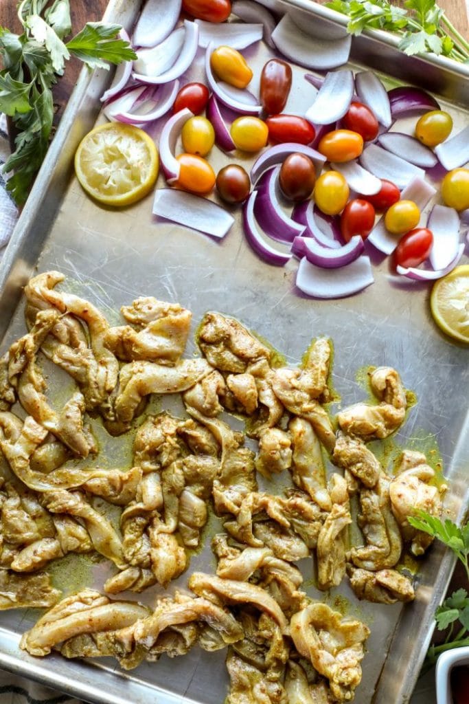 Sheet pan meal of raw chicken shawarma on one side and the veggies on the other. 