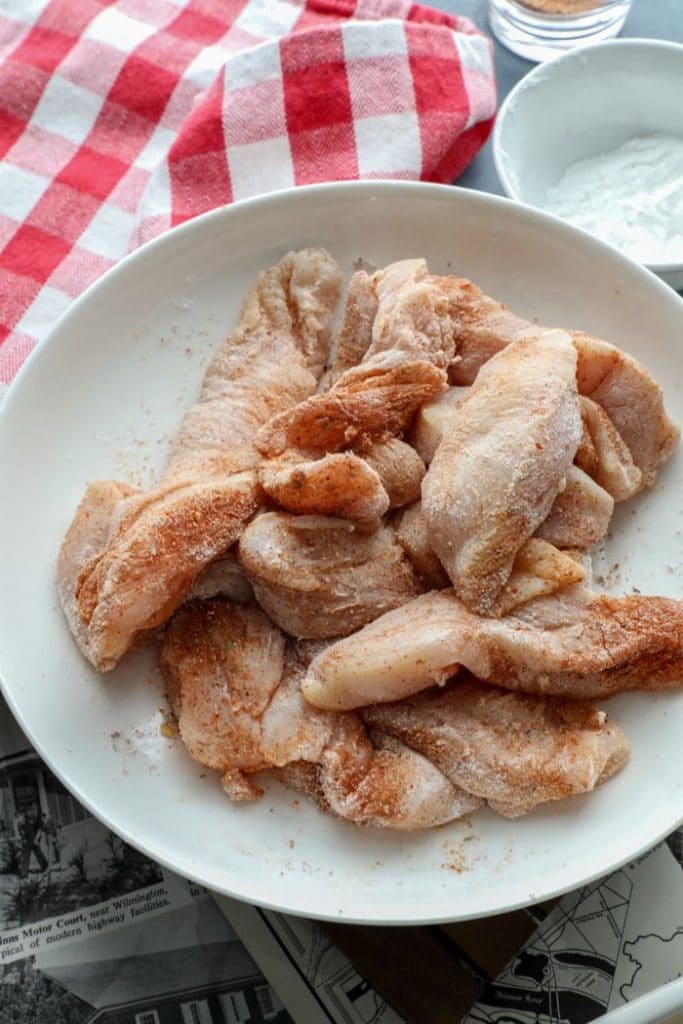 Raw chicken tender strips coated in Cajun spice and arrowroot powder in a bowl.
