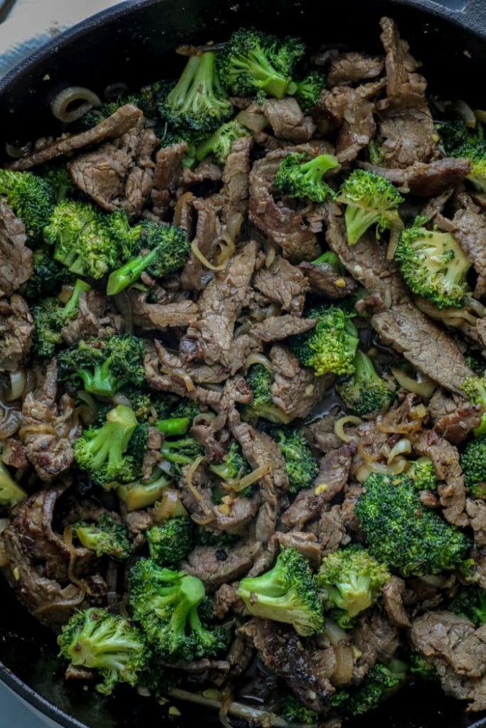 Beef and broccoli cooking in a cast iron pan. 