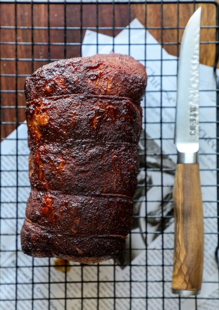 A whole smoked BBQ pork loin next to a knife.