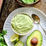 Avocado dressing in a bowl on a tray with an avocado next to it